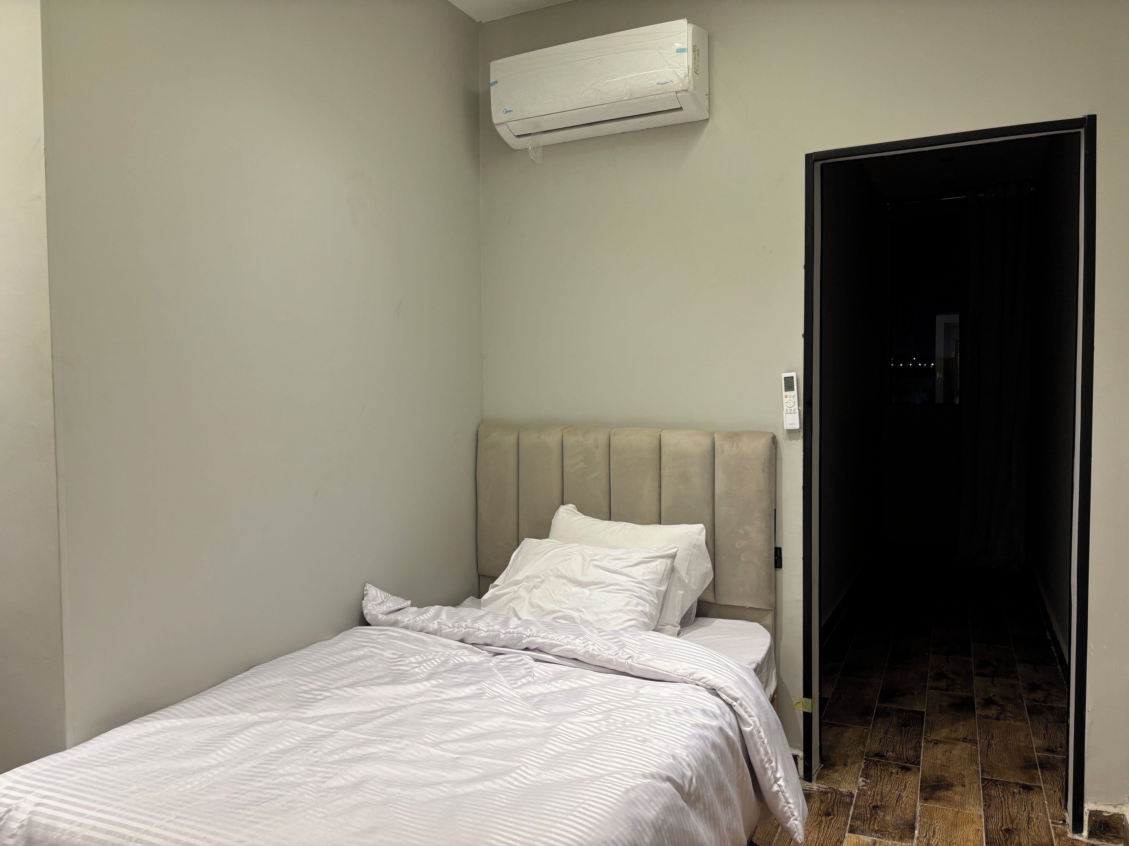 A small, neatly made bed with white linens in a room with light-colored walls and a wooden floor.