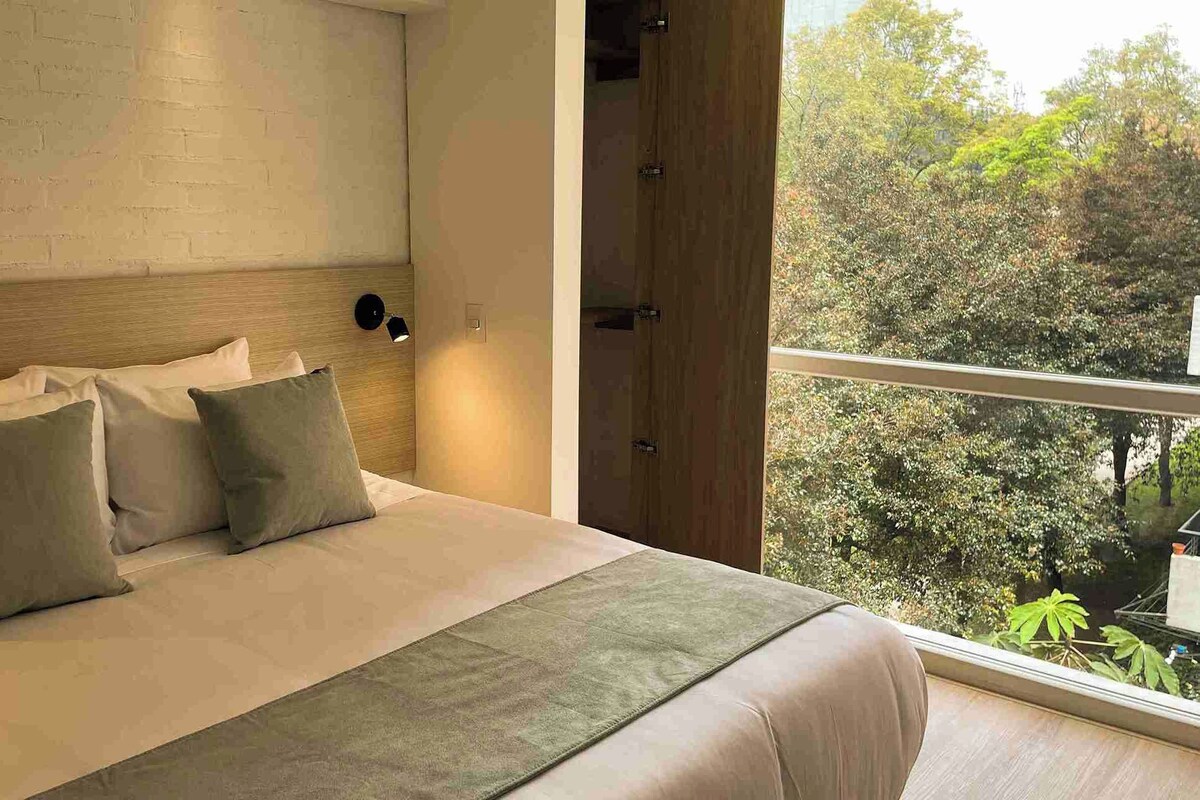 Ein Schlafzimmer mit einem großen Bett, einer Ziegelwand, einem Fenster mit Blick auf Bäume und einer Tür.