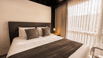 A hotel room with a large bed, two pillows, a bedside lamp, and a window with curtains.
