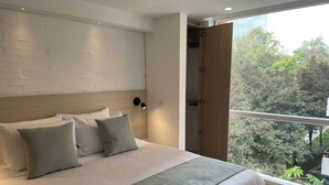 A modern bedroom with a large bed, a brick wall, a wooden door, and a view of trees. - Nova Iorque Suites by Avia Suites (Bogotá)
