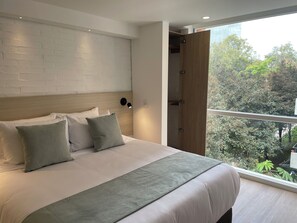 A modern bedroom with a large bed, a brick wall, a wooden door, and a view of trees. - Nova Iorque Suites by Avia Suites (Bogotá)