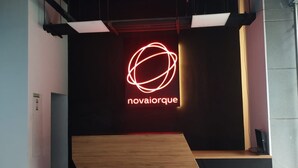 A modern interior with a neon sign reading 'novaiorque' on a dark wall, a wooden bench, and a sloped platform. - Nova Iorque Suites by Avia Suites (Bogotá)