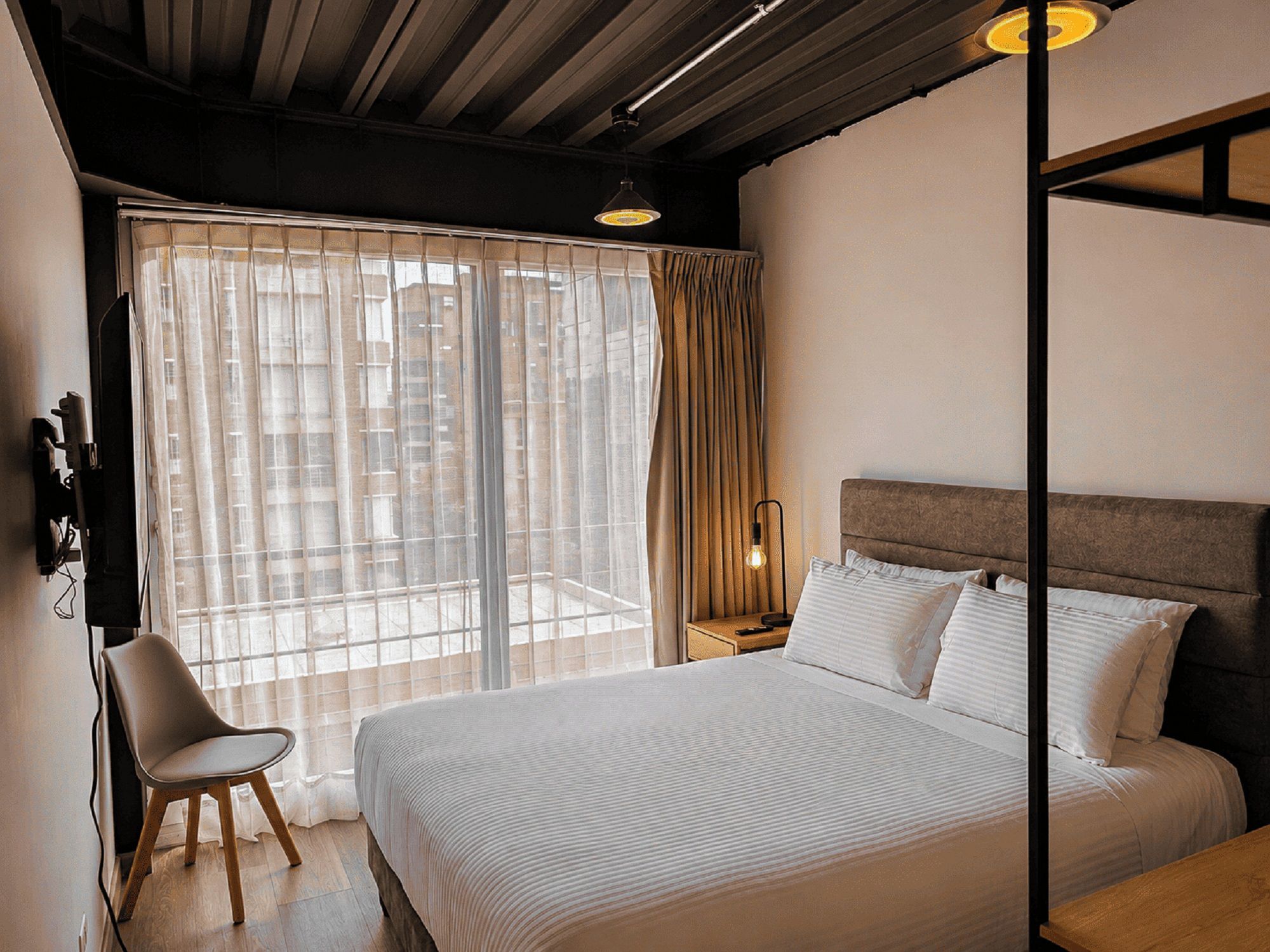 Una habitación de hotel con una cama grande, una silla, una mesita de noche y una ventana con cortinas.