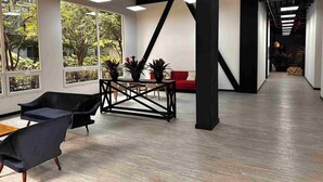 A spacious indoor area with large windows, a black metal table, and a red sofa. - Nova Iorque Suites by Avia Suites (Bogotá)