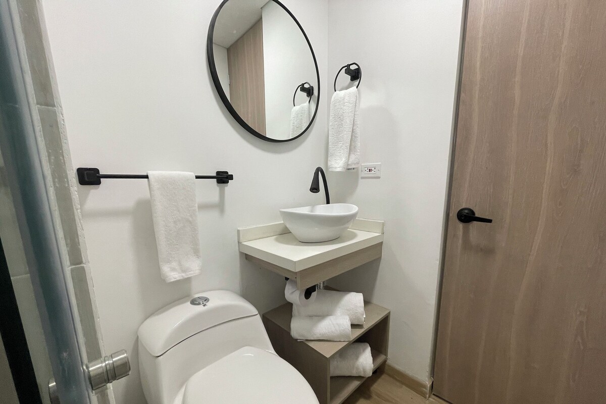 A bathroom with a toilet, sink, mirror, towel rack, and a door.