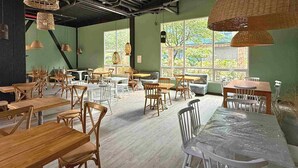 A spacious dining area with multiple tables and chairs, large windows with a view of greenery, and hanging wicker lamps. - Nova Iorque Suites by Avia Suites (Bogotá)