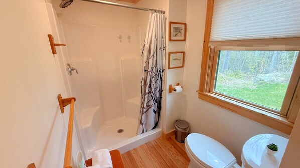 A bathroom with a shower, toilet, and window with a view of greenery.