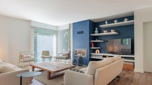 A modern living room with a sofa, chairs, a coffee table, and a TV area with shelves. - Villa Hortensia - Welkeys (Soorts-Hossegor)