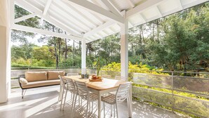 An outdoor patio with a wooden table and white chairs, surrounded by a white railing overlooking a garden. - Villa Hortensia - Welkeys (Soorts-Hossegor)