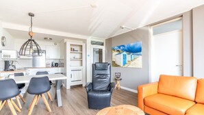 Een moderne woonkamer met een eethoek, een zwarte lederen fauteuil, een oranje bank en een schilderij aan de muur.