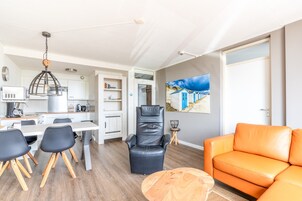 A modern living room with a dining area, a black leather chair, an orange sofa, and a painting on the wall.