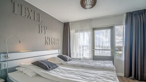Hotelkamer met twee bedden, een groot raam met gordijnen en een muur met de tekst 'TEXTEL BY NIGHT'.
