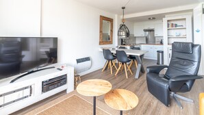 Een moderne woonkamer met een flatscreen televisie, een houten salontafel en een zwarte lederen fauteuil.