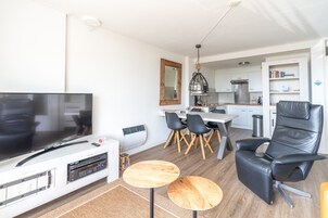 A modern living room with a flat-screen TV, wooden coffee table, and a black leather chair.