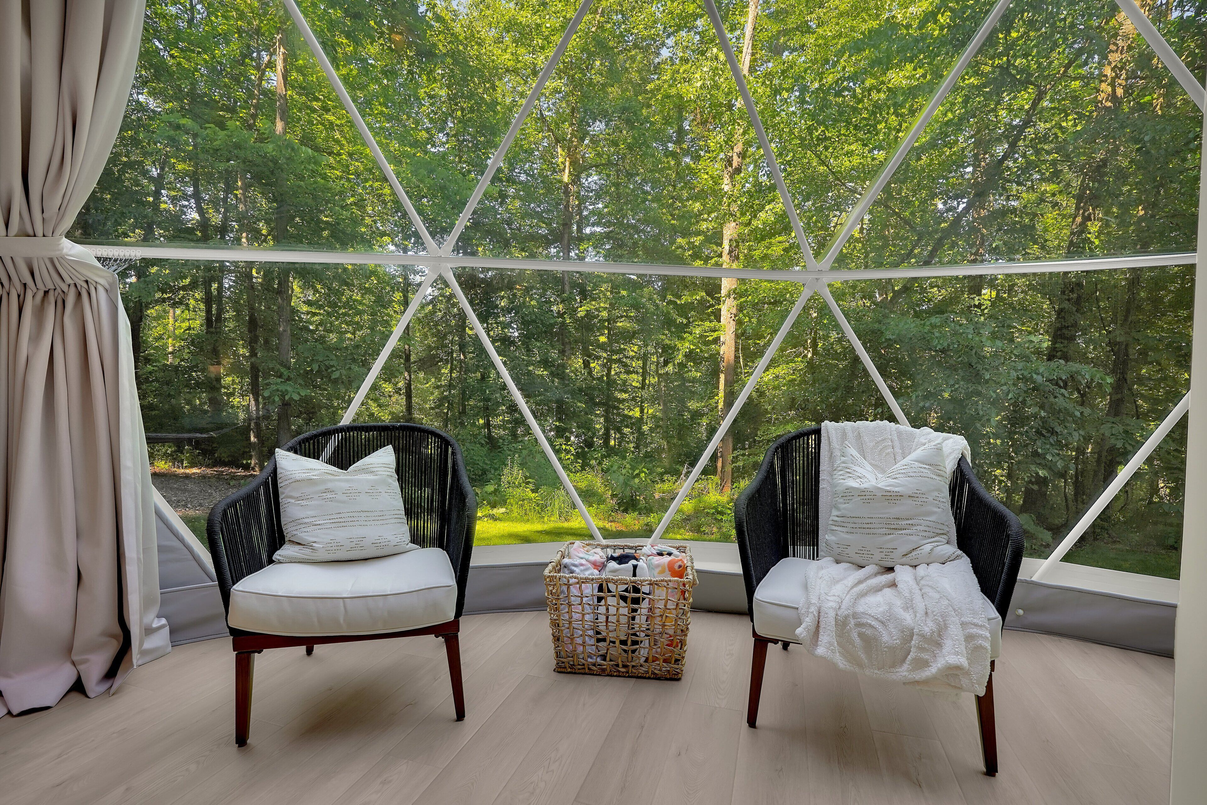 Ein Zimmer mit zwei Stühlen, einem Korb und Blick auf einen Wald durch eine geometrische Fensteranordnung.