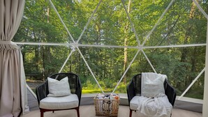 Una habitación con dos sillas, una cesta y vistas a un bosque a través de una estructura de ventana geométrica.
