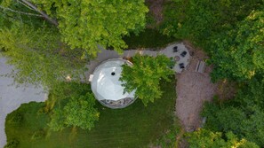 An aerial view of a gazebo with a circular roof, surrounded by a gravel area with seating and a fire pit.