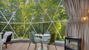 Una habitación con una cúpula de cristal, una mesa redonda con sillas, una mesita auxiliar negra con una lámpara y vistas a árboles a través de la cúpula.