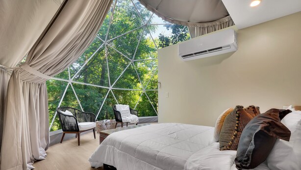 Un dormitorio con una cama grande, una silla y vistas a través de un ventanal geométrico.
