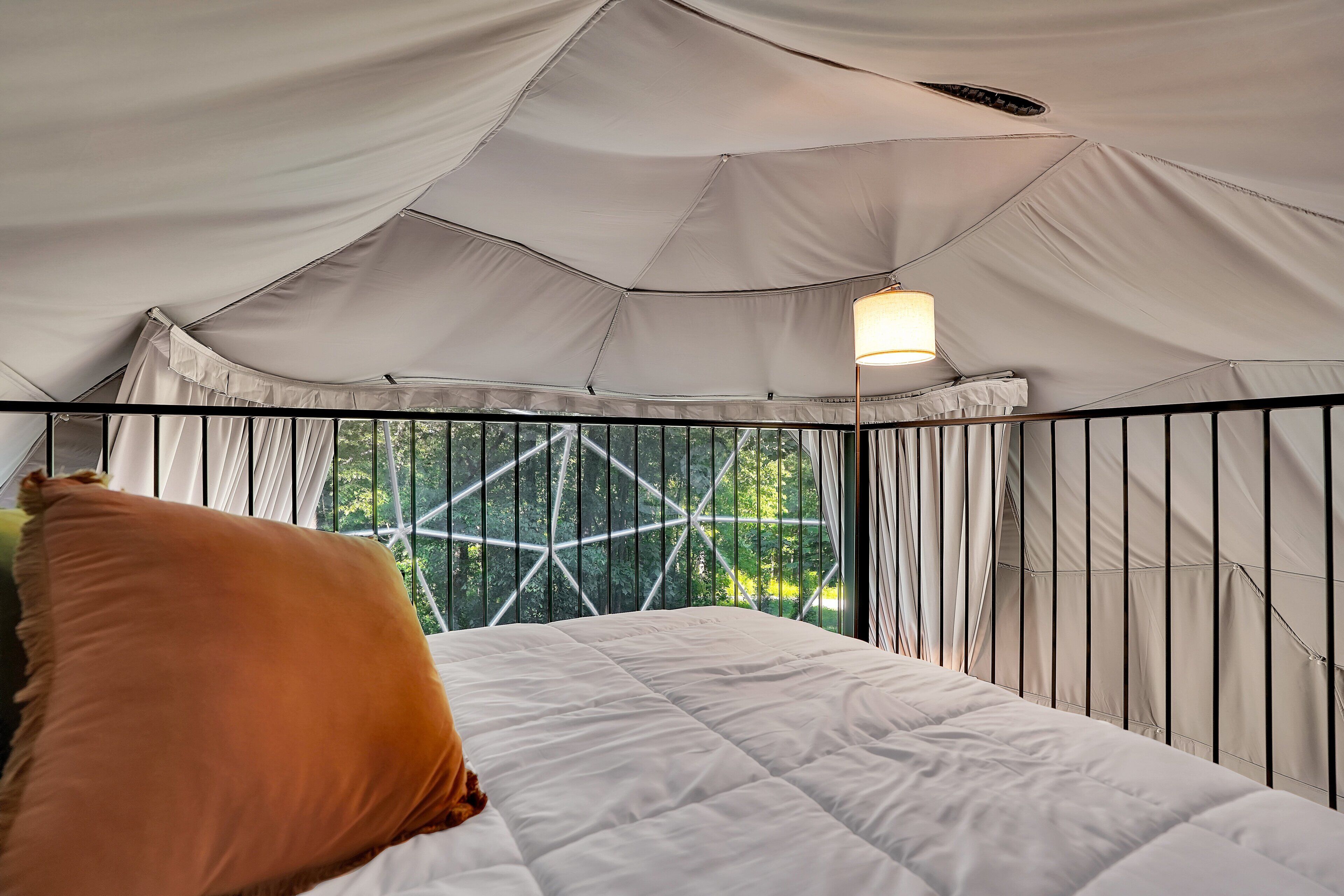 A tented room with a bed, a hanging light fixture, and a view through the window.