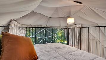 A tented room with a bed, a hanging light fixture, and a view through the window.