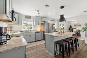 A modern kitchen with grey cabinets, a large island with stools, stainless steel appliances, and pendant lighting. - Private Pool + Hot Tub | Cottage on Bay (Sarasota)