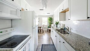 A modern kitchen with white cabinetry, a granite countertop, and a built-in stove. - Gardenia Cottage | In The Heart of Pinecraft! (Sarasota)