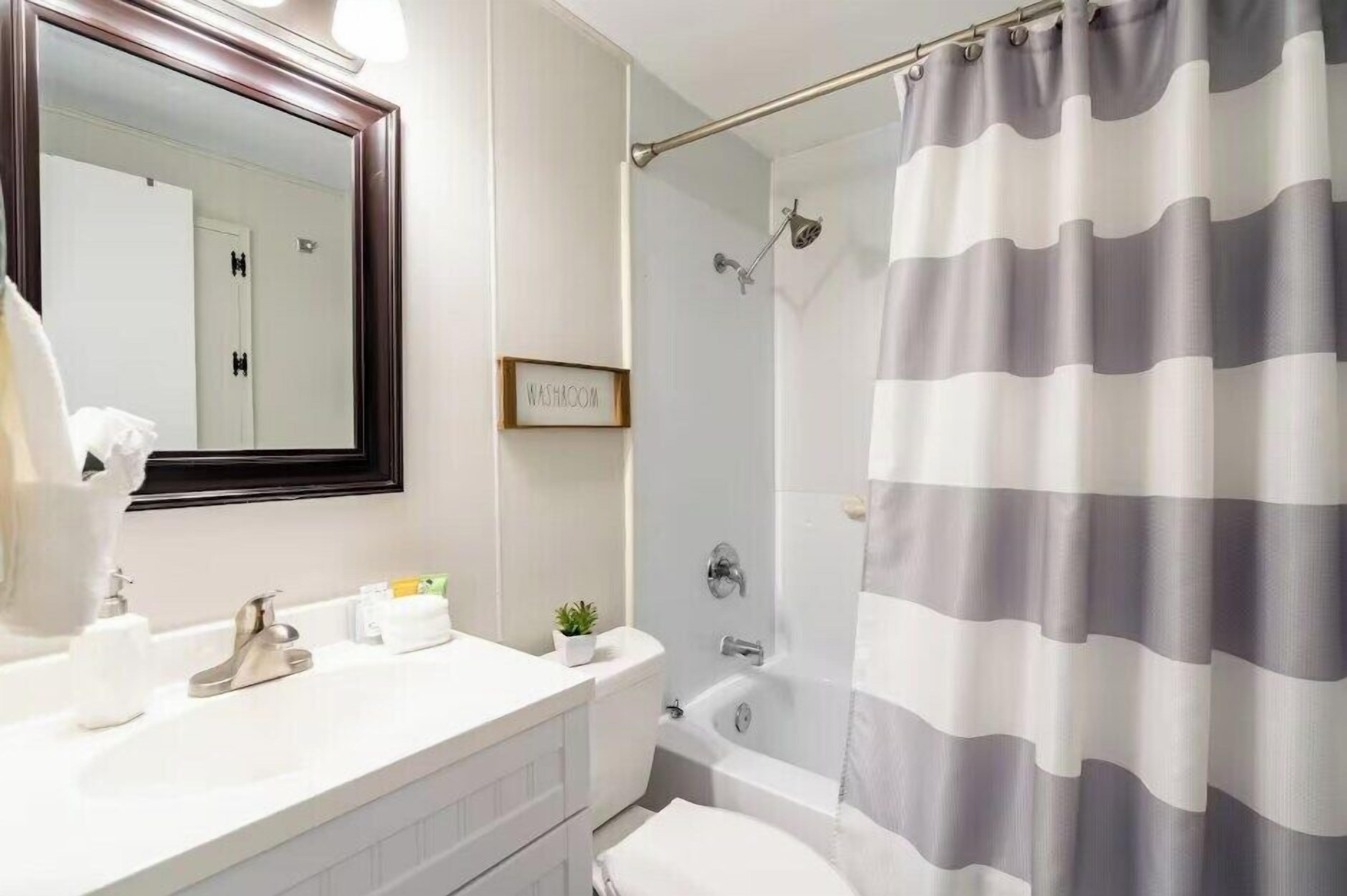 A bathroom with a white sink, a mirror, a toilet, and a shower curtain.