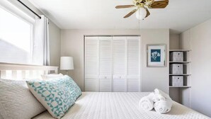 A bedroom with a bed, a ceiling fan, a window with curtains, a white wardrobe, and a framed picture on the wall. - Gardenia Cottage | In The Heart of Pinecraft! (Sarasota)