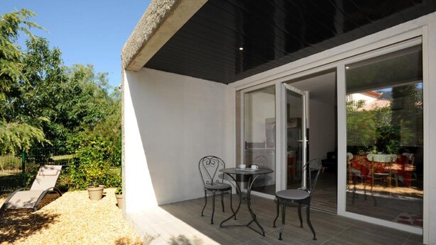 Un patio exterior con una mesa y sillas, un sillón de descanso y un ventanal de vidrio que da a un comedor.