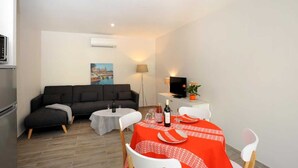 Un espacio habitable compacto con sofá, una mesa de comedor para dos, un televisor de pantalla plana y un cuadro en la pared.