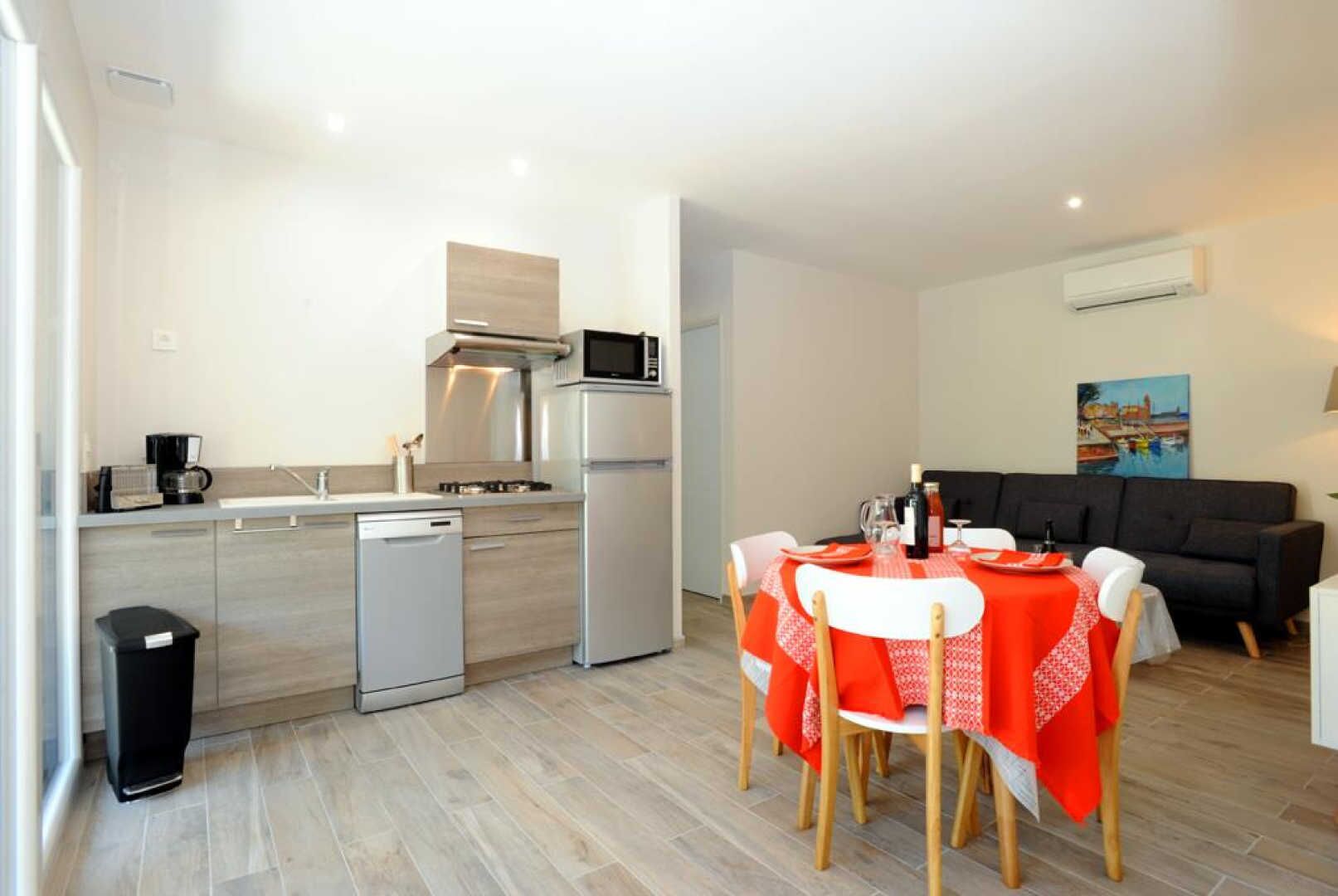 A modern kitchen with a dining area, including a table set for two with a red tablecloth.