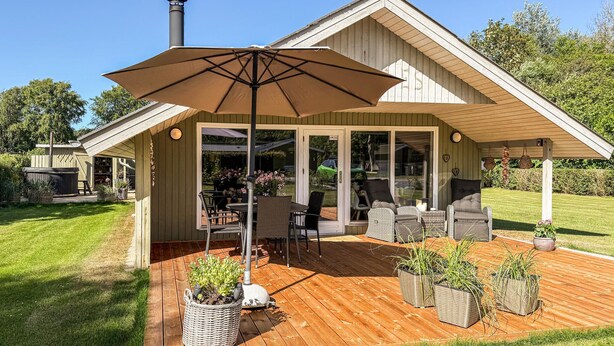 Een overdekt terras buiten, met een tafel, stoelen, een grote parasol en plantenpotten.