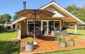 Eine überdachte Terrasse im Freien mit Tisch, Stühlen, einem großen Sonnenschirm und Pflanzen in Töpfen.