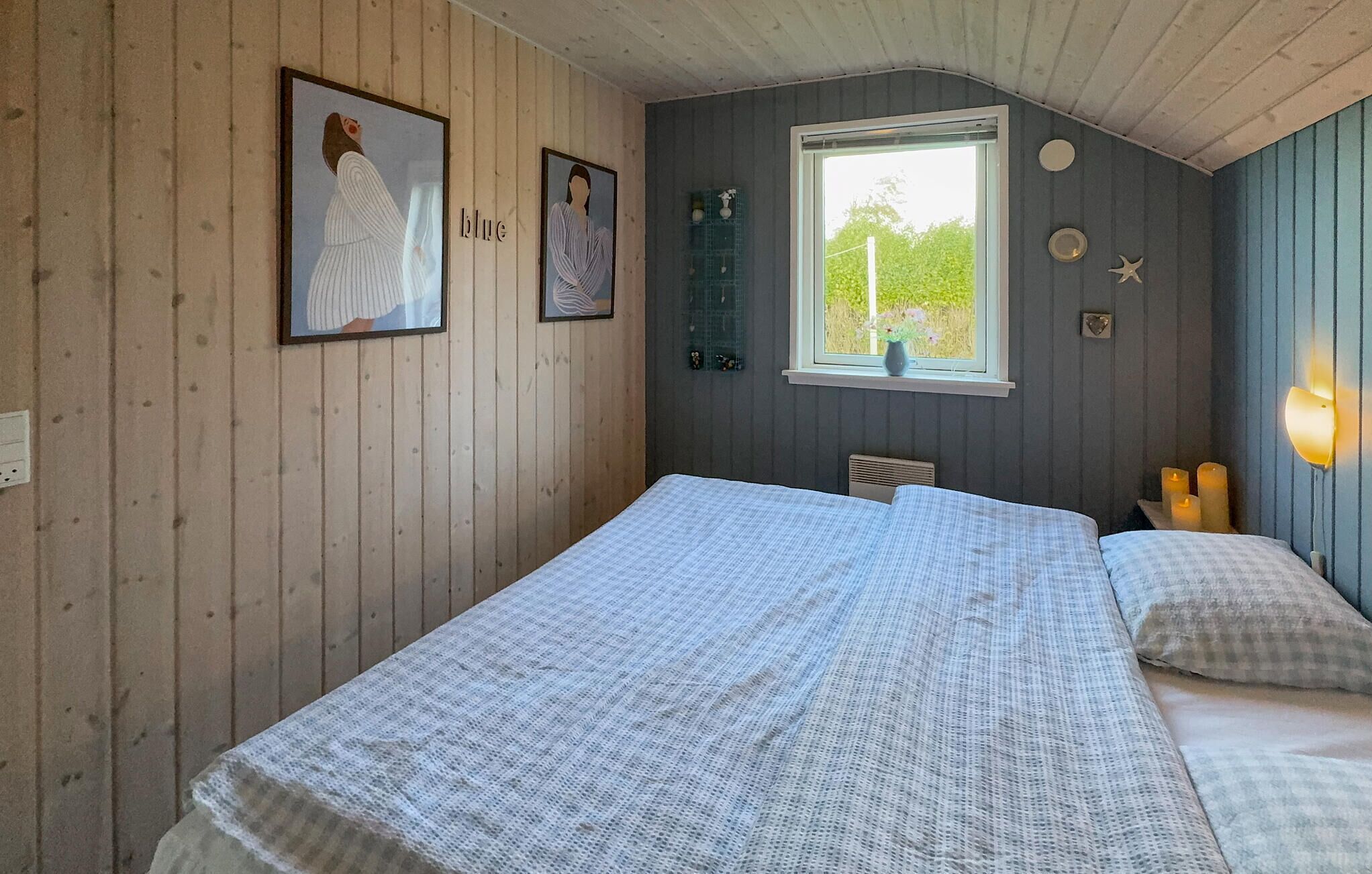 Quarto com teto de madeira, janela com vista para vegetação e duas camas com roupa de cama xadrez.