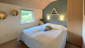 Een slaapkamer met een groot bed, een raam, een wandladder en een kleintje tafeltje met een plant.