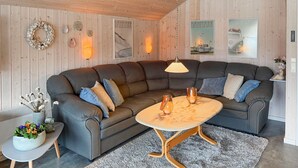 Een gezellige woonkamer met een donkergrijze modulaire bank, een ronde houten salontafel en een bijzettafeltje met een bloevas.