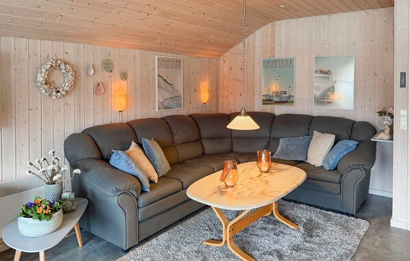 A cozy living room with a dark grey sectional sofa, a round wooden coffee table, and a small side table with a vase of flowers.