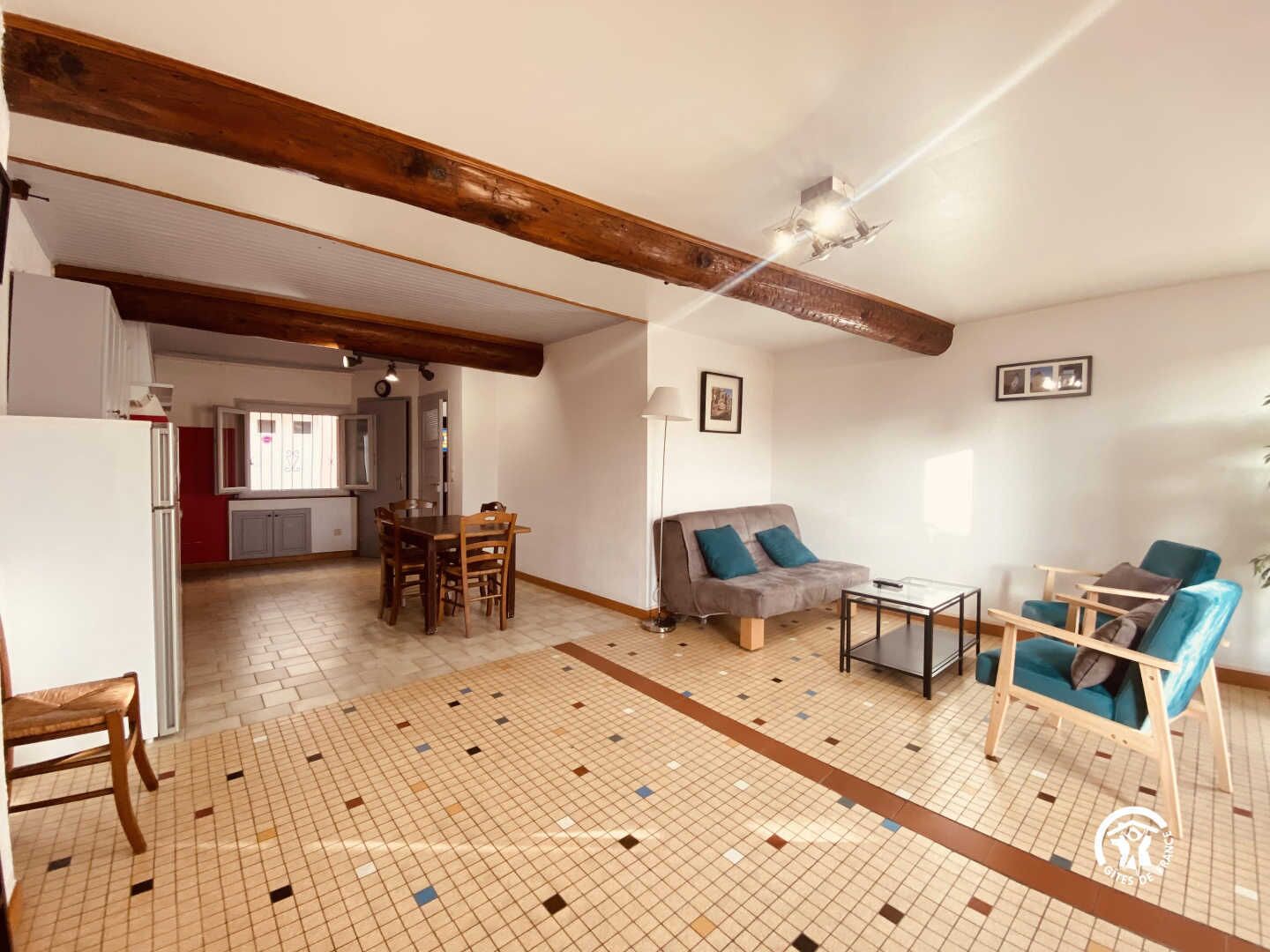 A spacious living area with a tiled floor, a wooden ceiling, a sofa, a coffee table, and a dining table with chairs.