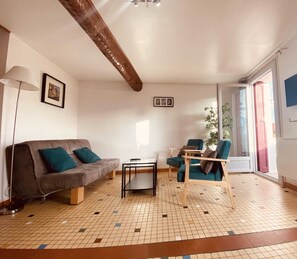 A living room with a sofa, a coffee table, and two chairs. There is a window with a view of the outside.