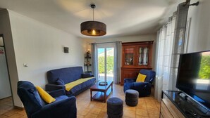 A living room with a sofa set, ottomans, a coffee table, a TV, and a fireplace. - Gîte Les Alicantes - BAGES (BAGES)