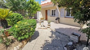 A courtyard with a tiled floor, surrounded by various potted plants and a stone planter. - Gîte Les Alicantes - BAGES (BAGES)