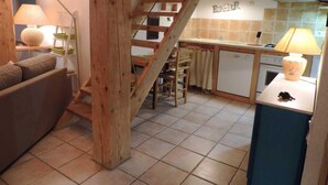A cozy living room with a sofa, a wooden staircase, a kitchen area with a stove, and a dining table.