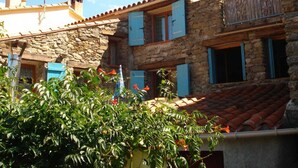 A stone building with blue shutters, a tiled roof, and a balcony.