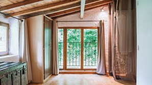 A room with wooden floors, a large window with a view of greenery, a rustic chest, and a wooden ceiling. - Le moulin - ST-LAURENT-DE-CERDANS (ST-LAURENT-DE-CERDANS)