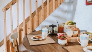 A wooden dining table with a chair, a wooden staircase, and a stone wall in the background. - Le moulin - ST-LAURENT-DE-CERDANS (ST-LAURENT-DE-CERDANS)