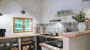 A kitchen with a wooden countertop, a sink, and a window with a view of greenery. There are shelves with kitchen items and a vase with flowers on the counter.
