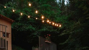 An outdoor dining area with a stone wall, two wooden chairs, a red table, and string lights. - Le moulin - ST-LAURENT-DE-CERDANS (ST-LAURENT-DE-CERDANS)