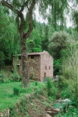 Un rustico edificio in pietra immerso nel verde e bagnato da un piccolo ruscello.
