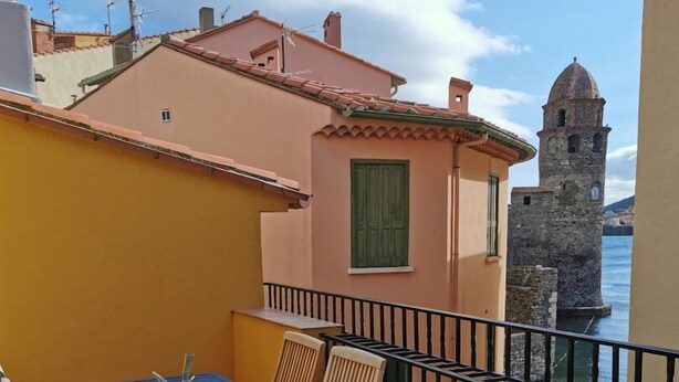 A balcony with a table and chairs, overlooking a body of water and a historic tower.